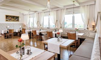 A bright restaurant area with large windows and elegant tables. The tables are decorated with flowers and candles, creating an inviting atmosphere.