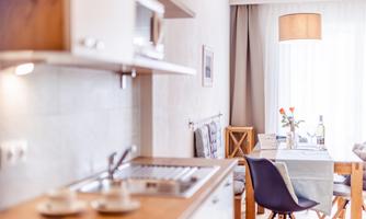 A modern kitchen with wooden details and a dining table. The space is bright and inviting, with natural light streaming in through the windows.