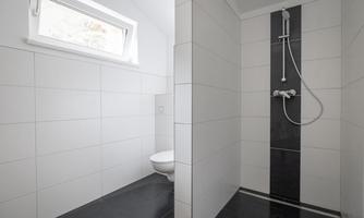 A modern bathroom with a shower and a toilet. The walls are decorated with white tiles and a dark stripe.