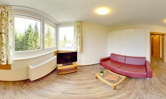 A modern living room with a red sofa and a television. Large windows let in a lot of light and offer a view of the trees outside.