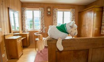 A cozy room with wooden paneling and large windows. A fabric sheep sits on a wooden barrier, adding a friendly touch to the ambiance.