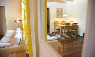A cozy living space with a white sofa and a dining area. The table is surrounded by wooden chairs, and the room has a bright, welcoming ambiance.