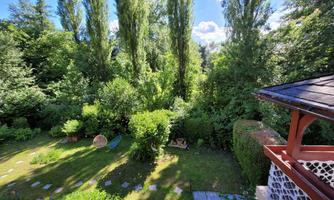 A green garden with many trees and shrubs. In the background, a small pavilion is visible.