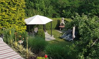 A beautiful garden with a seating area under a pavilion. Two loungers are ready to enjoy the tranquility of nature.