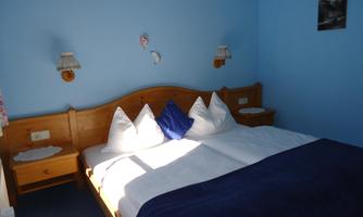 A cozy bedroom with a double bed and blue wall color. There are nightstands and lamps on the wall, as well as decorative pillows.