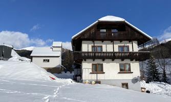 A snow-covered house in the mountains under a blue sky. The surroundings are quiet and idyllic.