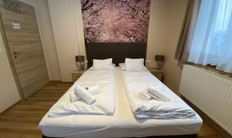 A modern bedroom with two separate beds. The walls are painted in a neutral tone and there is appealing wall decoration.