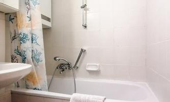 A simple bathroom with a bathtub and a shower. The room is bright and designed in a modern style.