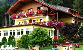 A charming house surrounded by colorful flowers and a well-maintained lawn. In the foreground are tables and chairs for a relaxing stay outdoors.