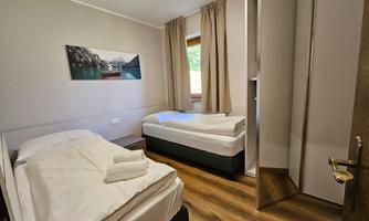 A simple room with two single beds and a large window. The walls are light, and a picture of a mountain landscape hangs on the wall.