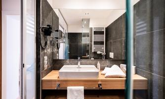 A modern bathroom with a stylish wooden bathtub and elegant black tiles. Bright lighting and a clear glass shower give the space an inviting atmosphere.
