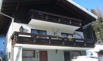A charming chalet in the snow with a large balcony and wooden decorations. The surroundings are wintry and idyllic.
