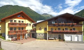 A beautiful hotel building in the mountains with wooden cladding and blooming balconies. The surroundings are green and offer a picturesque view.