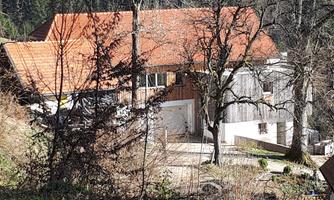 A rustic house with a red roof in a natural setting. Surrounded by forest, it features wood and stone architecture.