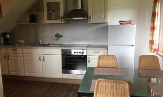 A modern kitchen with white cabinets and a silver hood. Three chairs are at the table, and the window has colorful curtains.