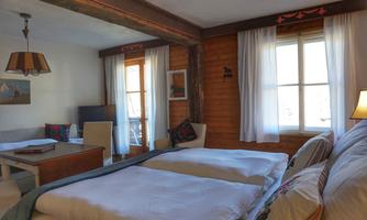 A cozy bedroom with two single beds and a wood-paneled wall design. Large windows provide plenty of daylight and a welcoming atmosphere.