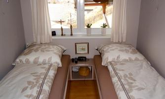 A cozy bedroom with two single beds and light curtains. Through the window, a peaceful view of the surroundings is visible.