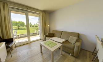 A bright living room with a cozy sofa and a table. Large windows offer a view of the garden.