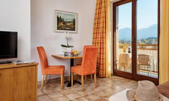 A cozy living kitchen with a small dining area and orange chairs. Large windows offer a view of the mountains and the balcony.