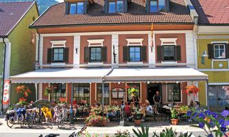 A charming restaurant with a large terrace full of plants and guests. Bicycles are parked along the street, and the colorful façade of the building gives the place an inviting character.