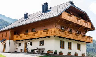A beautiful, modern house in alpine style with wooden cladding and a large balcony. Surrounded by green mountains and a clear atmosphere.