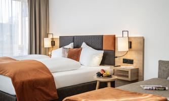 A cozy hotel room with a double bed and modern lamps. The warm colors and the small table with fruit create an inviting atmosphere.