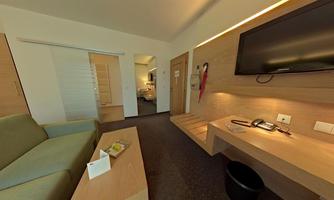 A modern hotel room with a cozy sofa and a desk. A television hangs on the wall, and there is a view of the entrance of the room.