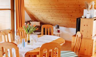 A cozy dining area with a round wooden table and chairs. On the table is a vase with fresh tulips and decorative elements.