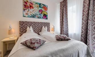 A cozy bedroom with two single beds and elegant bedding. The walls are adorned with colorful pictures and curtains.