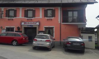 A pink building with a sign displaying the name "Gasthof." Several cars are parked in front of the house.