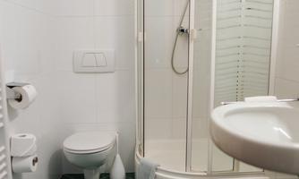 A small bathroom with a shower cabin, sink, and toilet. The floor is tiled with green tiles.