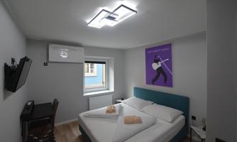 A modern room with a large double bed and a workspace. An artwork hangs on the wall and there is a window with daylight.