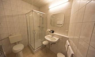 A simple bathroom with white tiles. It features a shower, a sink, and a toilet.