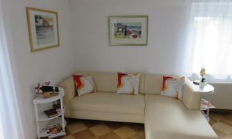 A modern living room with a bright, comfortable couch and colorful pillows. Pictures hang on the wall, and light streams through the window.