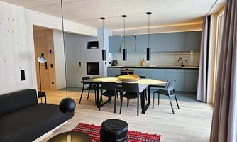 A modern living room with an open kitchen. The space is bright and inviting, furnished with a dining table and stylish furniture.