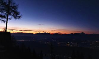 A picturesque sunset over the mountains with soft colors in the sky. Silhouettes of trees and mountains create a serene atmosphere.