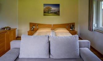 A cozy room with two beds and a sofa in the foreground. A picture of a landscape hangs on the wall.