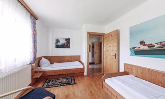 A simple room with two single beds and a cozy seating area. Bright walls and large windows create a friendly atmosphere.