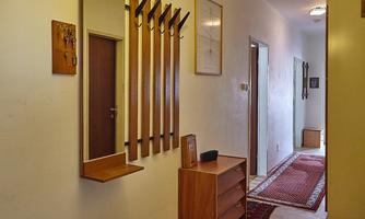 A narrow hallway with a wooden mirror and several coat hooks. Also visible are a dresser and a carpet.