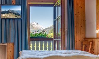 A cozy room with an open window that offers a view of the mountains. In the background, curtains and a television are visible.