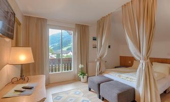 A cozy bedroom with a view of the mountains. It is bright and friendly with a large window and elegant furnishings.