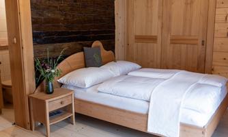 A cozy bedroom with a wooden bed and fresh bedding. Next to the bed is a nightstand with a small vase and flowers.