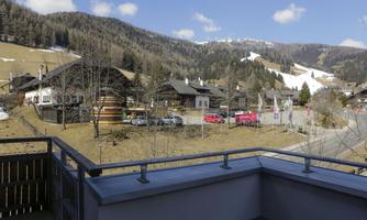 A soothing mountain landscape with traditional chalets. The sun is shining and the sky is blue with a few clouds.