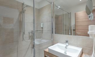 A modern bathroom with a shower and a sink. The walls are in neutral tones, and there is plenty of natural light.