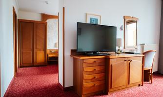 A cozy hotel room with wooden furniture and a television on a dresser. The room has a red carpet and access to another room.