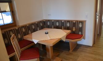 A cozy dining area with a wooden bench and a table. The walls are painted in light colors, and the seat covers are adorned with a beautiful pattern.
