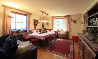 A cozy dining area with a large table and comfortable chairs. The room is bright and welcoming, with windows and traditional decorations.