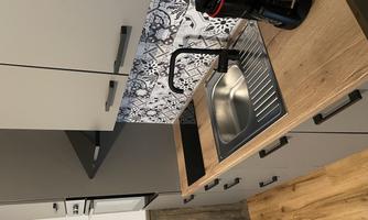 A modern kitchen with a stainless steel sink and a black faucet. In the background, a stylish tiled wall and a coffee machine can be seen.