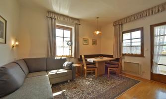 A cozy living room with a gray sofa and a wooden table. Bright windows provide plenty of daylight in the room.