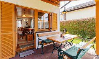 An inviting terrace with a table and benches. The view leads into the interior of a cozy house with warm light.
